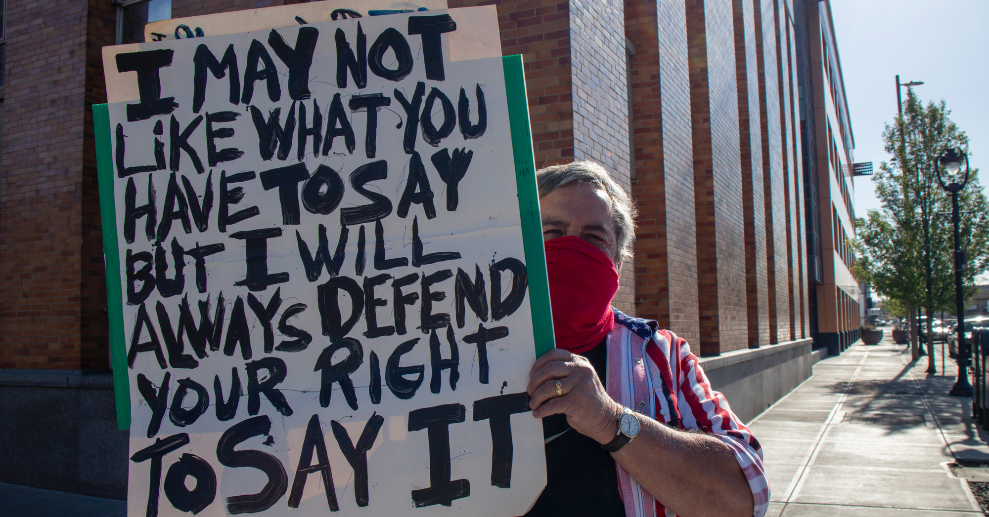 Image of Jason White supporter outside Yakima City Hall holding sign saying, "I may not like what you have to say, but I will always defend your right to say it."