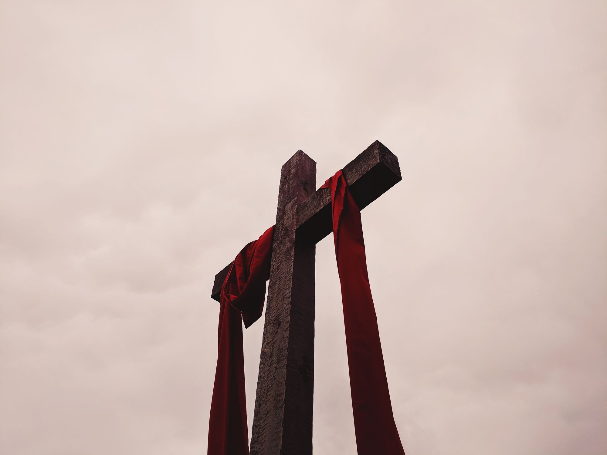 Christian cross with red ribbon draped over it.